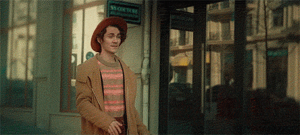 A goofy man in a red hat walks down the street before doing a big leap in the air